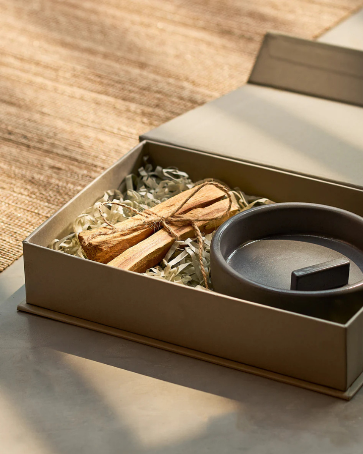 Open box containing a black ceramic dish and Palo Santo on a wooden surface